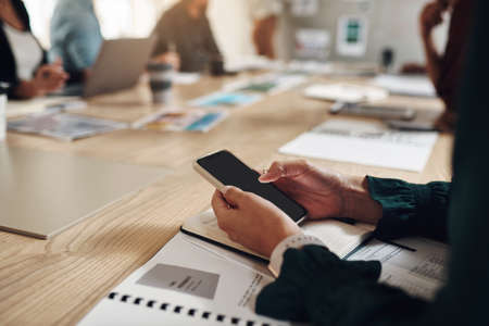 Easiest way to take notes. an unrecognizable businesswoman using her cellphone while sitting in the boardroom.の写真素材