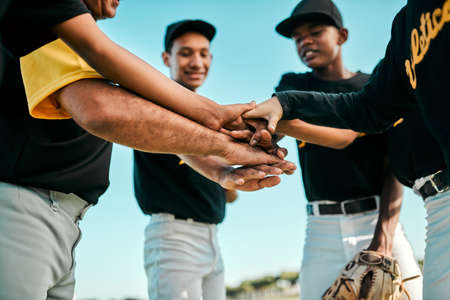 No one player can dominate the game. a team of young baseball players joining their hands together in a huddle during a game.の写真素材