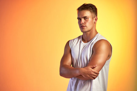 Fitness is a confidence builder. Studio portrait of a handsome young male athlete standing with his arms folded against an orange background.の写真素材