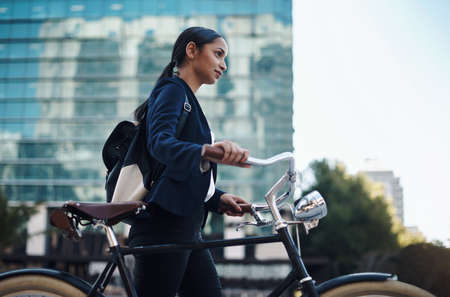 Keep going and youll get there. a young businesswoman traveling with a bicycle through the city.の写真素材