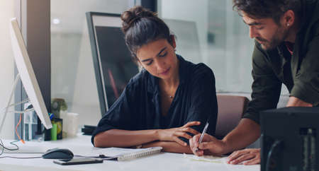 Helping her with the details. two young businesspeople working together in the office.の写真素材