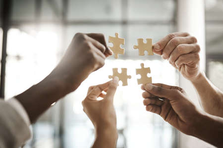 Diverse team solving a problem together due to teamwork, support and helping each other in the office. Group of business people assembling a puzzle and collaborating in unityの写真素材
