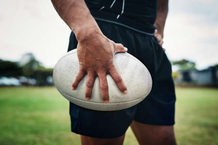 Playing with this ball is his favourite thing. an unrecognizable rugby player holding a rugby ball on the field during the day.の写真素材