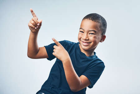 Check it out, yo. Studio shot of a cute little boy pointing against a grey background.