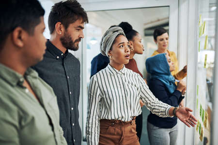 Discussing the big plans they all have. a group of businesspeople brainstorming with notes on a glass wall in an office.の写真素材