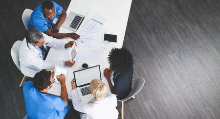 Unity, teamwork and brainstorming by health care workers researching online while having a meeting in conference room. Overhead of doctors browsing the internet to help find cure or medical solutionの写真素材