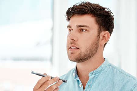 Sending a quick voice note. a handsome young businessman recording a voice note while siting at a...