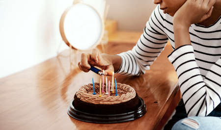 Everybody forgot my birthday. a woman lighting candles on a birthday cake at home and looking sad.の写真素材