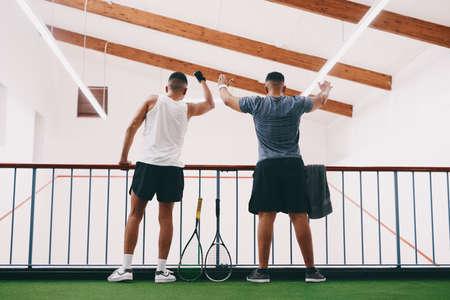 Whats sport without its fans. Rearview shot of two young men cheering while watching a game of squash from the viewing gallery.の写真素材