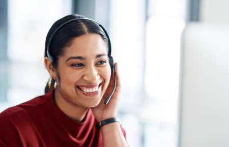 Shes so smooth and persuasive over the phone. a young businesswoman wearing a headset while working on a computer in an office.の写真素材
