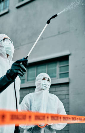 Healthcare workers wearing hazmat suits disinfecting a building during covid pandemic. First responders spraying virus protection sanitizer or cleaning to prevent the spread of germs and for hygieneの写真素材