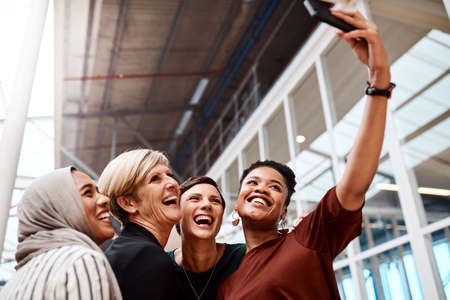 You can just tell that they have the utmost confidence. Portrait of a group of businesswomen taking selfies together in an office.の写真素材
