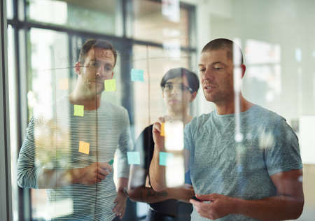 Businesspeople in brainstorm, thinking and planning session in a modern office. Creative team sharing ideas and strategy for collaboration at the workplace. Young group of designers in teamwork plan.の写真素材
