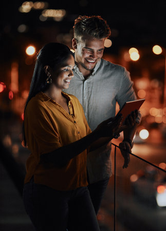 Making success all theirs. two businesspeople using a digital tablet together outside an office at night.の写真素材