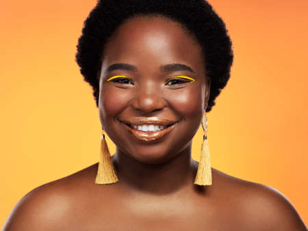 Gold really is my colour. Studio shot of a beautiful young woman posing against an orange background.の写真素材