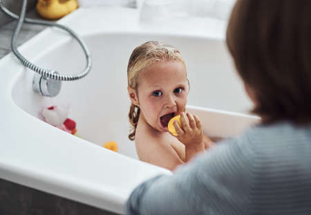 Can I stay in here. an adorable little girl bonding with her mother while taking a bath at home.