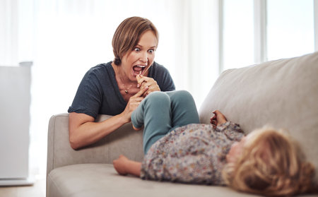Im going to eat your toes. an attractive young mother and playing with her daughter in the living room at home.の写真素材