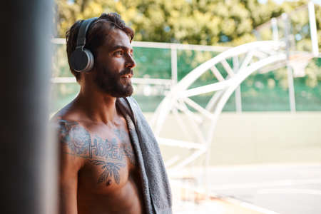 This day is yours to conquer. a sporty young man listening to music while standing against a fence outdoors.の写真素材