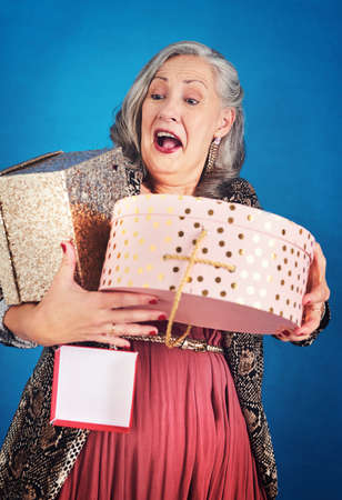 The gifts keep coming in. a cheerful senior woman holding boxes of gifts and presents in studio.