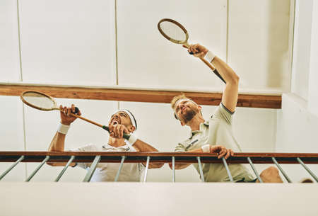 Youll find the winners at the top. two young men watching a game of squash from the viewing gallery.