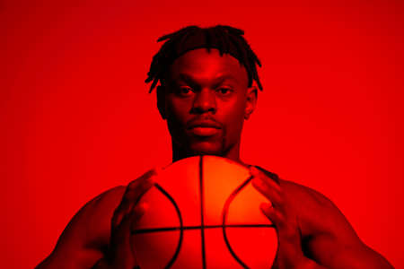 Keep your head in the game. Red filtered shot of a young sportsman posing with a basketball in the studio.の写真素材