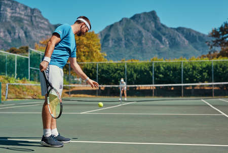 It never gets easier, you just get better. Full length shot of a young male tennis player getting ready to serve the ball on a tennis court outdoors.の写真素材