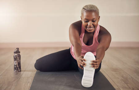 Stretching out my legs post workout. Full length shot of an attractive young woman sitting alone and...