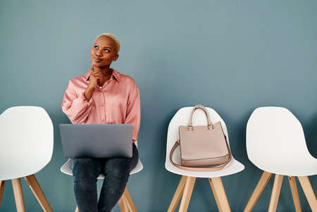 Should I do what Im thinking. Studio shot of an attractive young businesswoman looking thoughtful while using a laptop against a grey background.の写真素材