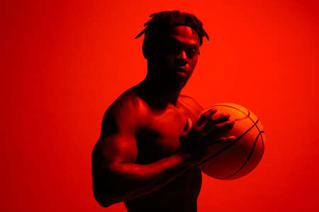 Expect great things of yourself. Red filtered shot of a young sportsman posing with a basketball in the studio.の写真素材