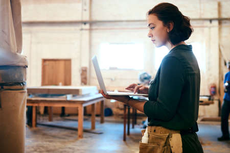 I want to try some of these designs. a female carpenter using a laptop in her workshop.