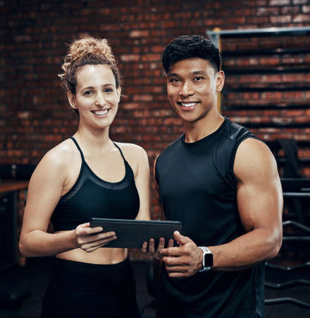 Check out our website for awesome workout routines. two sporty young people holding a digital tablet in the gym.の写真素材