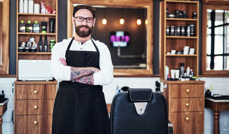 His service is a cut above the rest. Portrait of a handsome young barber posing with his arms folded inside a barbershop.の写真素材