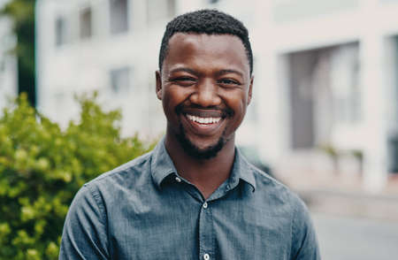 This is the smile of success. Cropped portrait of a handsome young businessman sitting alone outside during the day.の写真素材