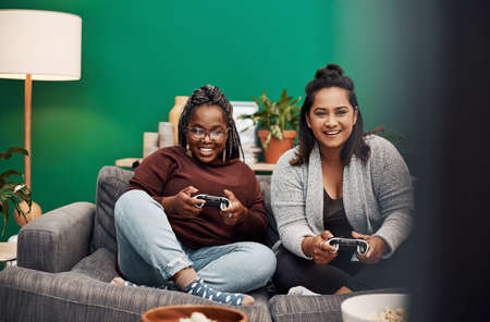 Its not a game without my girl. two young women playing video games on the sofa at home.の写真素材