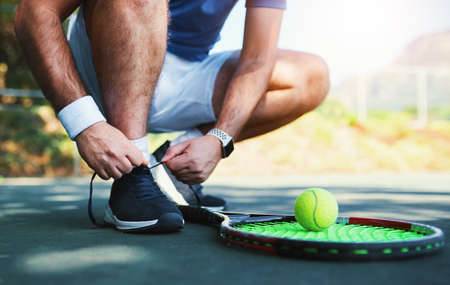 Laced up and ready to do battle. an unrecognizable male tennis player tying his shoelaces outdoors on a tennis court.の写真素材