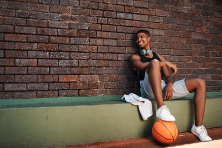I believe in shooting for your goals. a sporty young man taking a break after a game of basketball.の写真素材