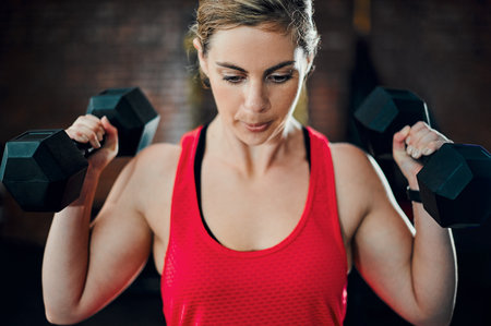 Its time to get those muscles working. an attractive young female athlete working out with dumbbells in the gym.の写真素材