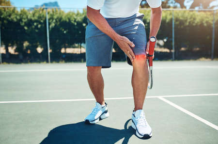 Ow My knee. an unrecognizable sportsman suffering from a knee injury while playing tennis alone.の写真素材