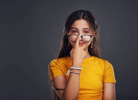 We call it fashion. Cropped portrait of an attractive teenage girl wearing glasses and standing against a dark background in the studio alone.の写真素材