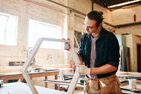 Just making sure everything fits perfectly. a handsome young carpenter working on a wooden frame inside a workshop.の写真素材