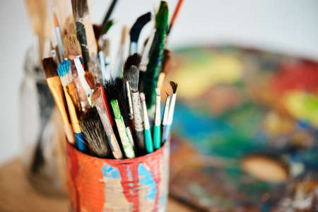 Lets get painting. a tin full of paintbrushes in an empty art studio after a painting class.の写真素材