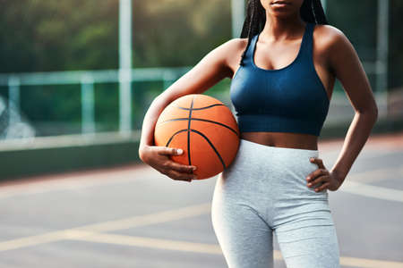 I belong on the court. an unrecognizable sportswoman standing on the court alone and holding a basketball during the day.の写真素材