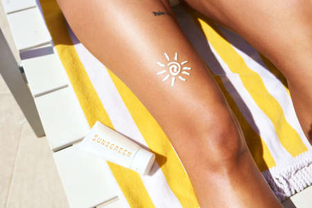 an unrecognizable woman wearing sunscreen while relaxing outside on a lounger.