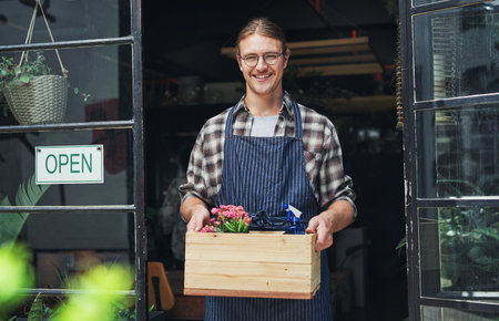 Ready for business. Cropped portrait of a handsome young business owner holding a crate of flowers at the entrance of his floristry.の写真素材