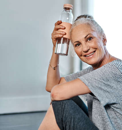 That was a great yoga session. Portrait of a cheerful mature woman practicing yoga while having a drink of water inside of a studio during the day.の写真素材