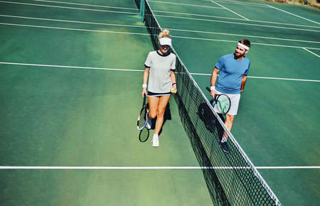 Which side are you on. Full length shot of two young tennis players talking while walking together outdoors on a tennis court.の写真素材