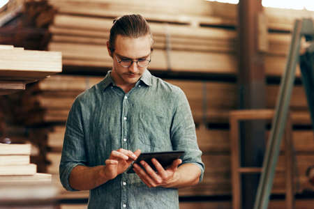The fastest way to grow your business is to go online. a young carpenter using a digital tablet while working inside his workshop.の写真素材