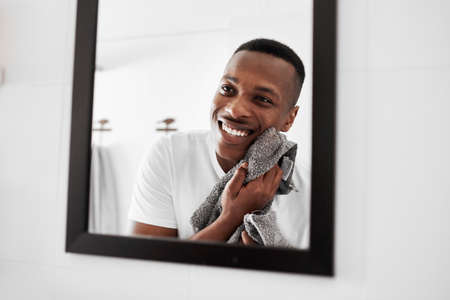 This new product that Im using is really working. a man looking into the mirror while drying his face with a towel.の写真素材