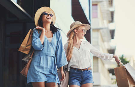 Who doesnt love a little shopping spree. two attractive young girlfriends laughing while walking with shopping bags in the city during the day.の写真素材