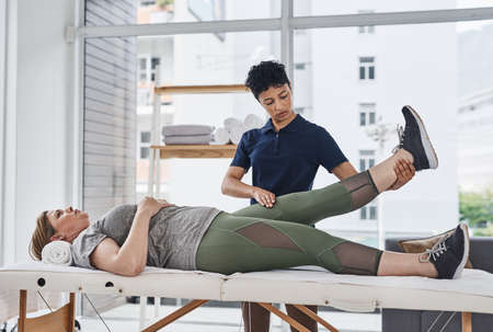 Shes committed to bringing you back to full health. a young physiotherapist doing leg exercises with...